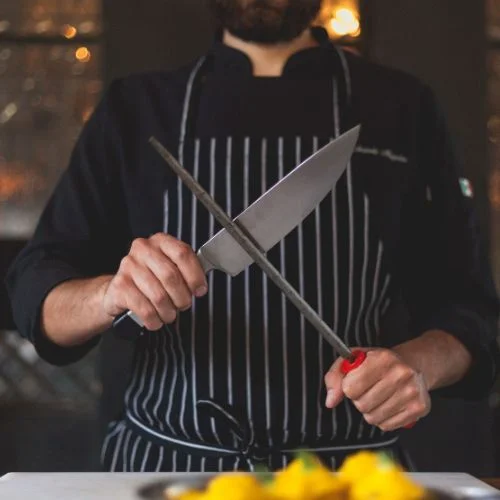Professional chef sharpening knives representing precision and craftsmanship in food industry partnerships
